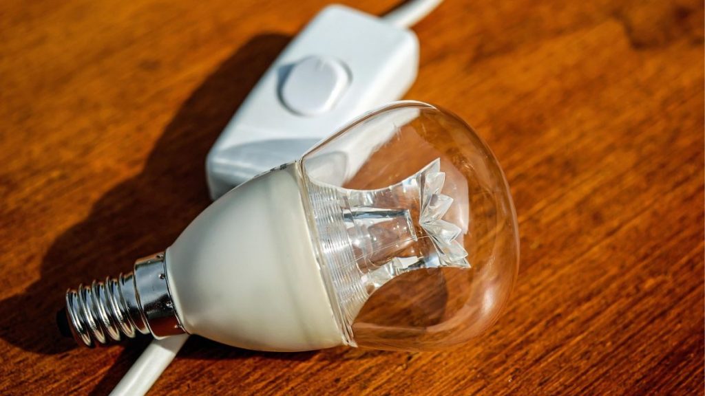 Primer plano de una bombilla de luz pequeña junto a un interruptor blanco sobre una superficie de madera.